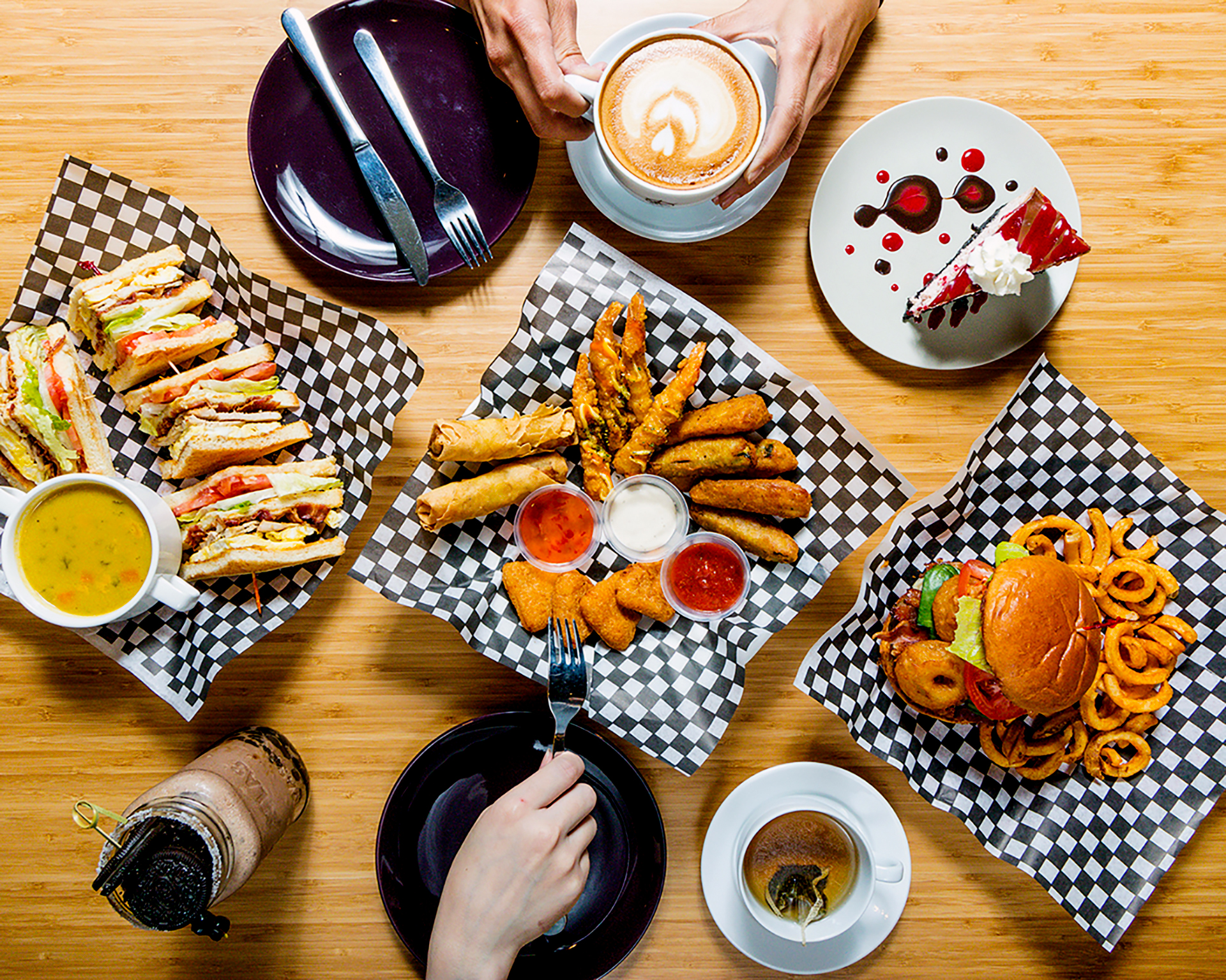 A Charisma table shared with sandwiches, appetizers, a burger, coffee and cheesecake